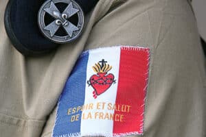 Écusson du drapeau français avec un Sacré-Cœur brodé sur la manche. Dans le passant de la chemise un béret avec la croix scout.